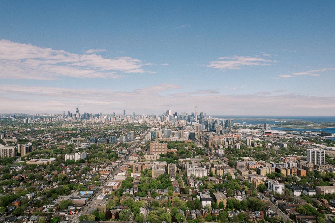 Aerial view of Toronto skyline with CN Tower, cityscape showcasing urban and green areas, clear blue sky overhead.