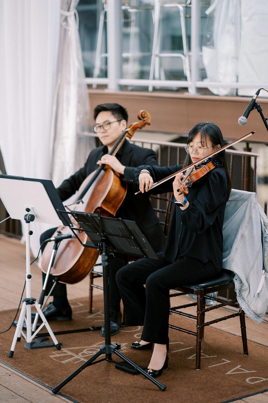 String duo performing at an event, featuring a cellist and a violinist in elegant black attire, playing classical music indoors.