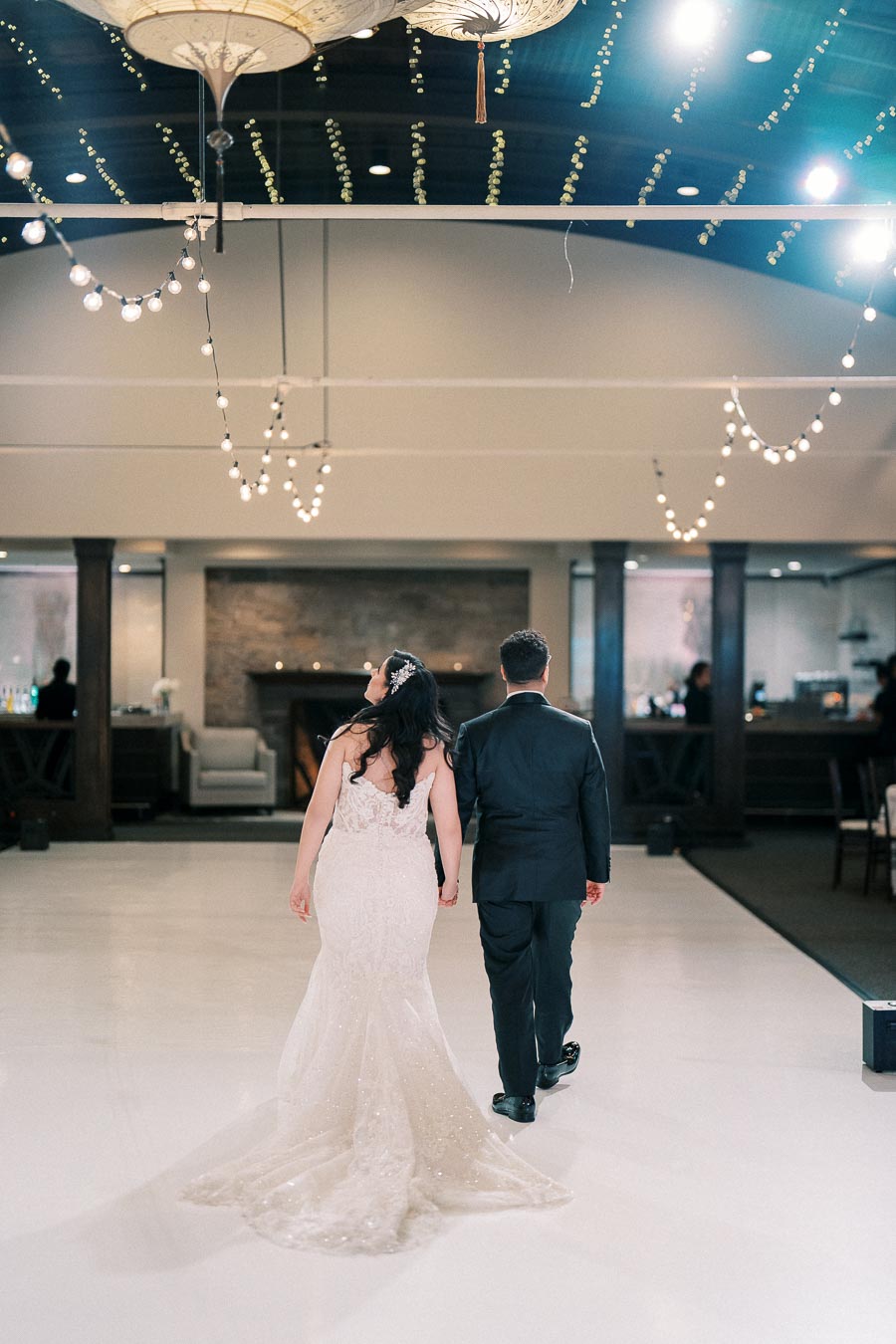 A bride and groom walk hand-in-hand across a beautifully decorated wedding venue, featuring elegant lighting and a sophisticated interior.