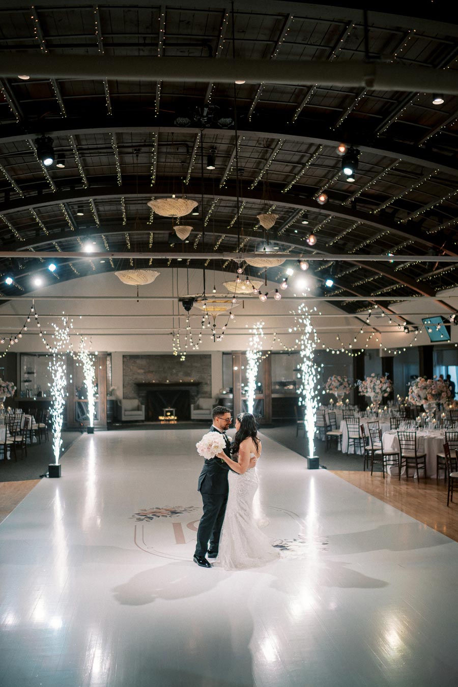 A couple shares a romantic first dance at their wedding reception, surrounded by elegant décor and sparkling light displays in a beautifully lit venue.