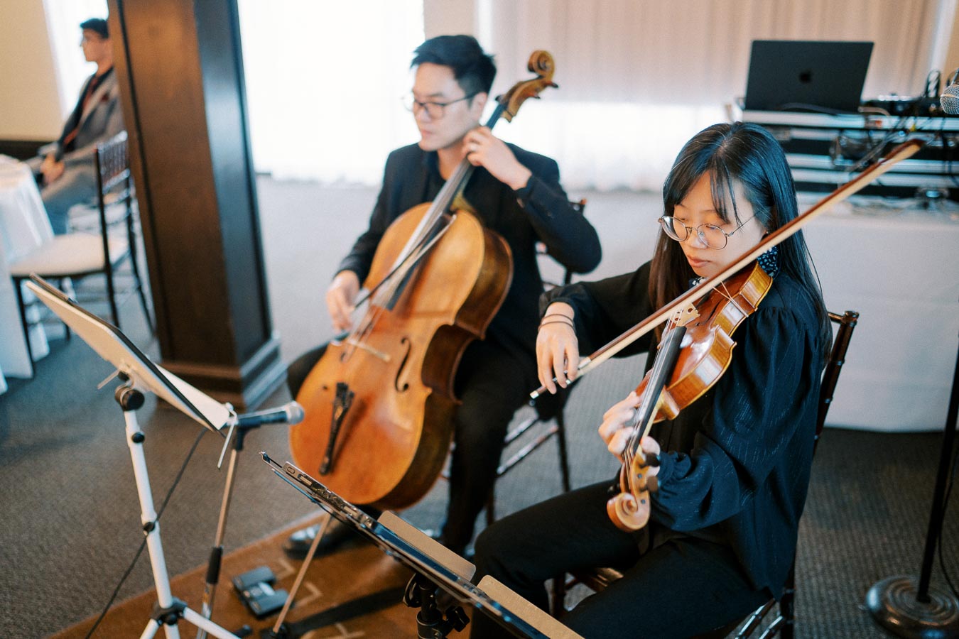 Two musicians performing classical music; a violinist and a cellist seated indoors during a live performance.