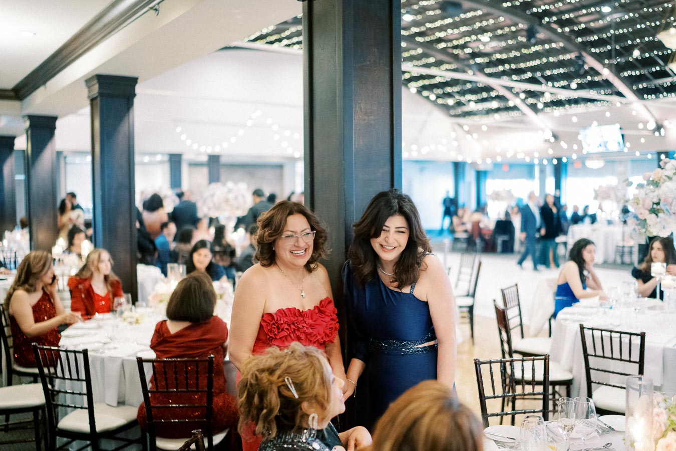 Guests enjoying a lively social gathering at a beautifully decorated banquet hall, featuring elegantly set tables and festive lighting.