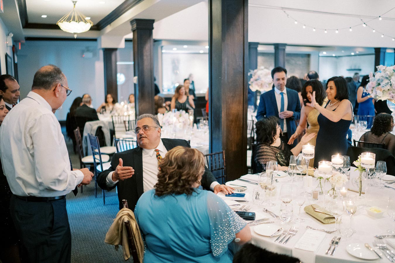 A lively wedding reception with guests mingling and chatting around a decorated dinner table.