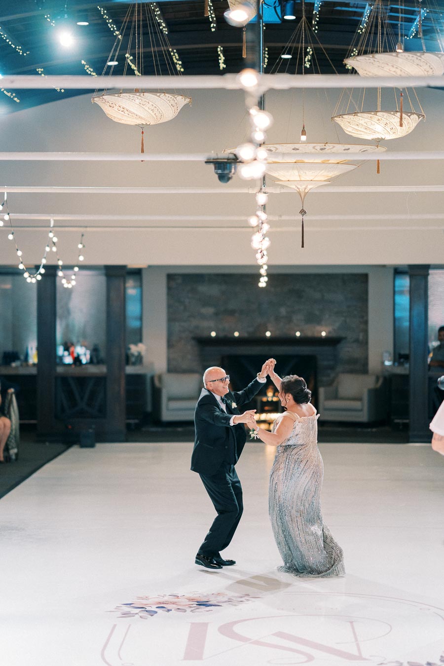 Elegant couple dancing at a decorated indoor wedding venue, featuring shimmering outfits and ambient lighting for a romantic atmosphere.