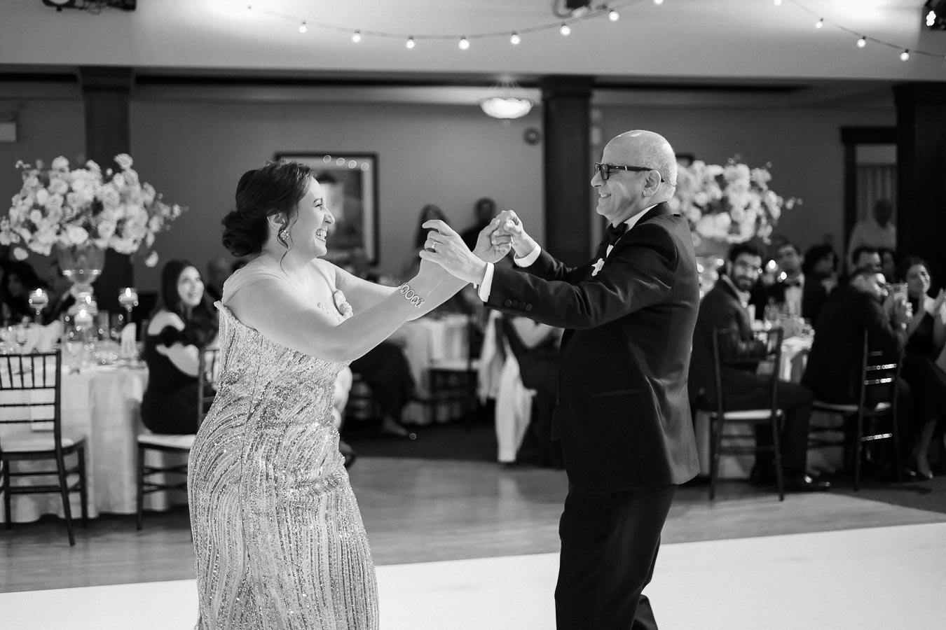 Father and daughter joyfully dancing at wedding reception, surrounded by elegantly decorated tables and guests.