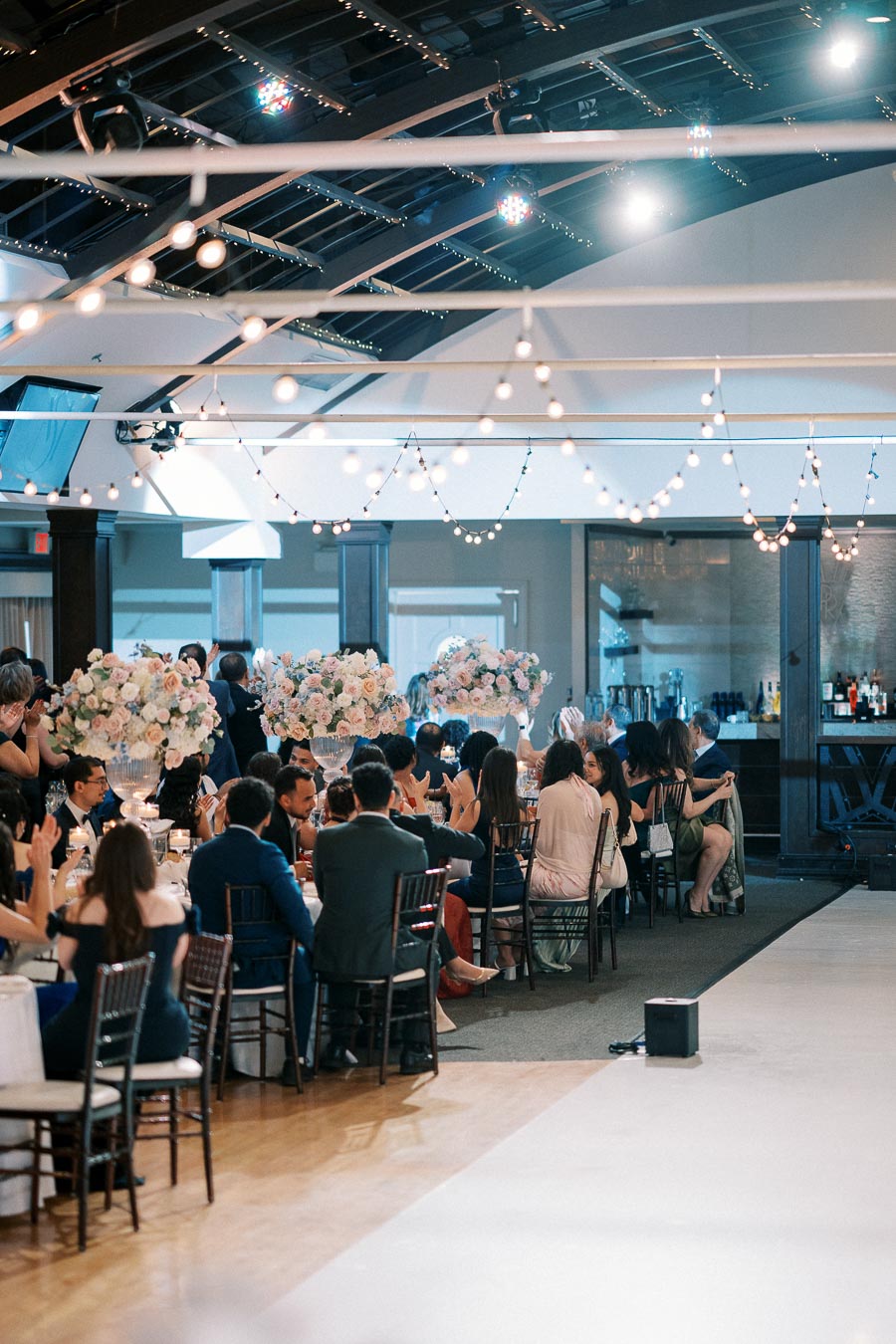 Guests seated at elegantly decorated tables during a wedding reception, with string lights and floral centerpieces creating a romantic ambiance.