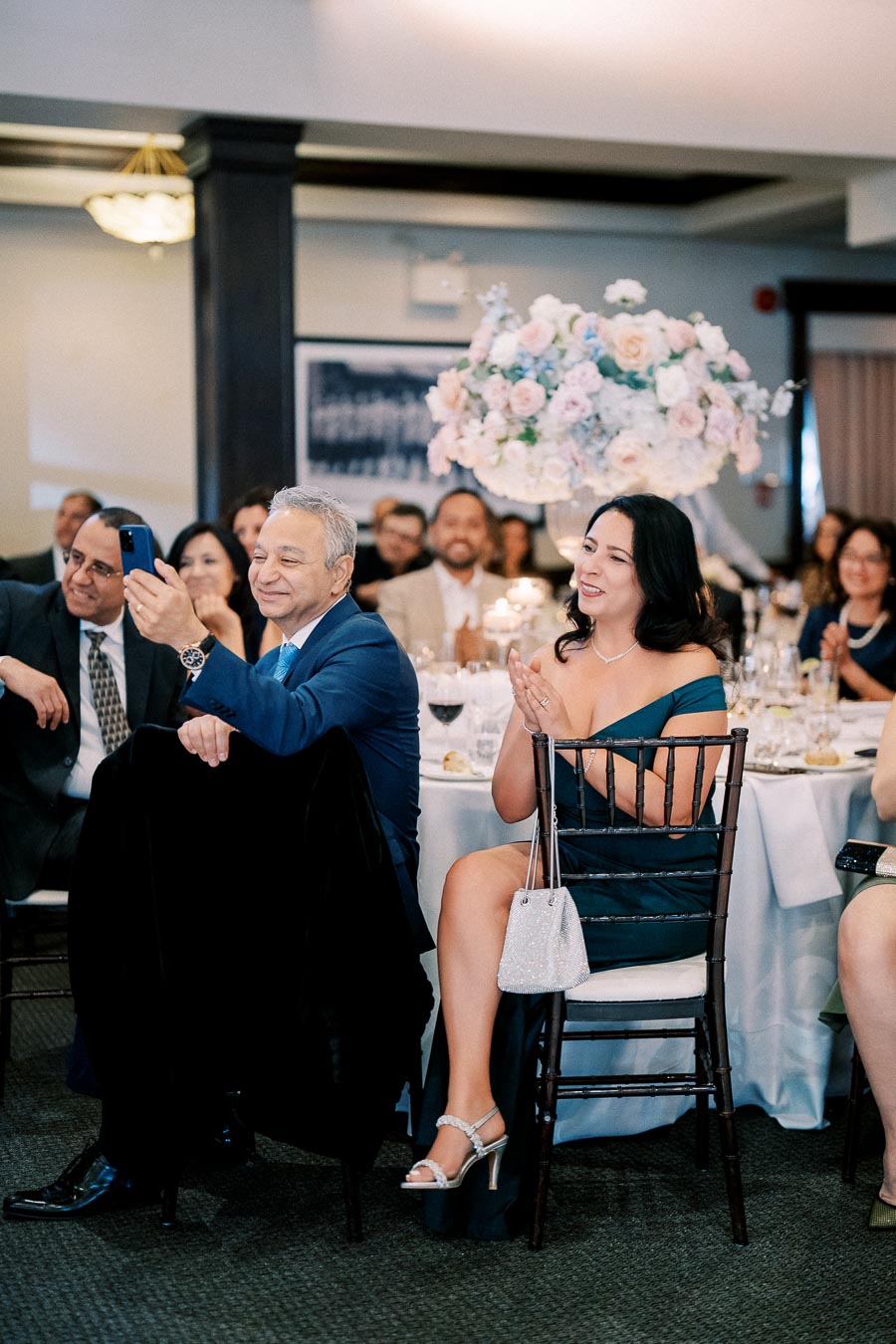 Guests smiling and engaging at a festive wedding reception, with elegantly decorated tables and floral centerpiece.