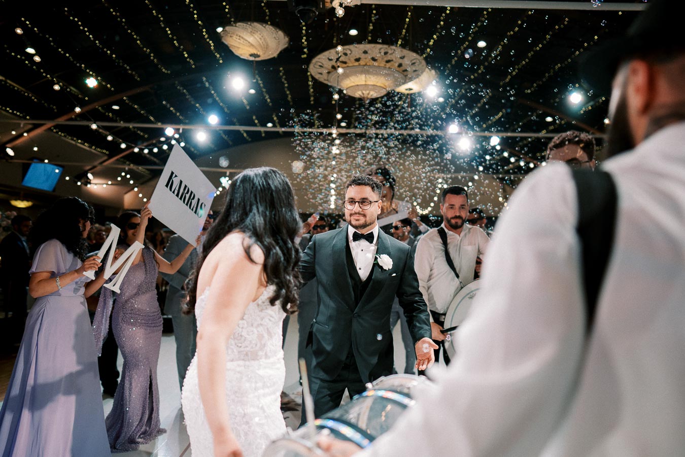 Wedding celebration with couple dancing surrounded by guests, confetti, and musicians in a beautifully decorated venue.