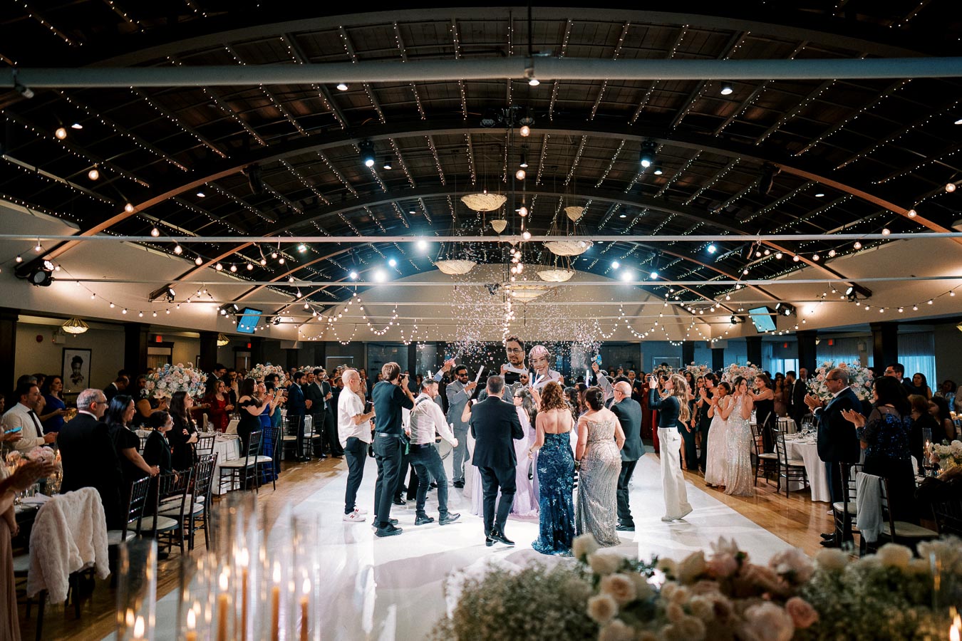 Wedding reception with guests dancing under elegant string lights in a beautifully decorated venue, celebrating a joyful occasion.