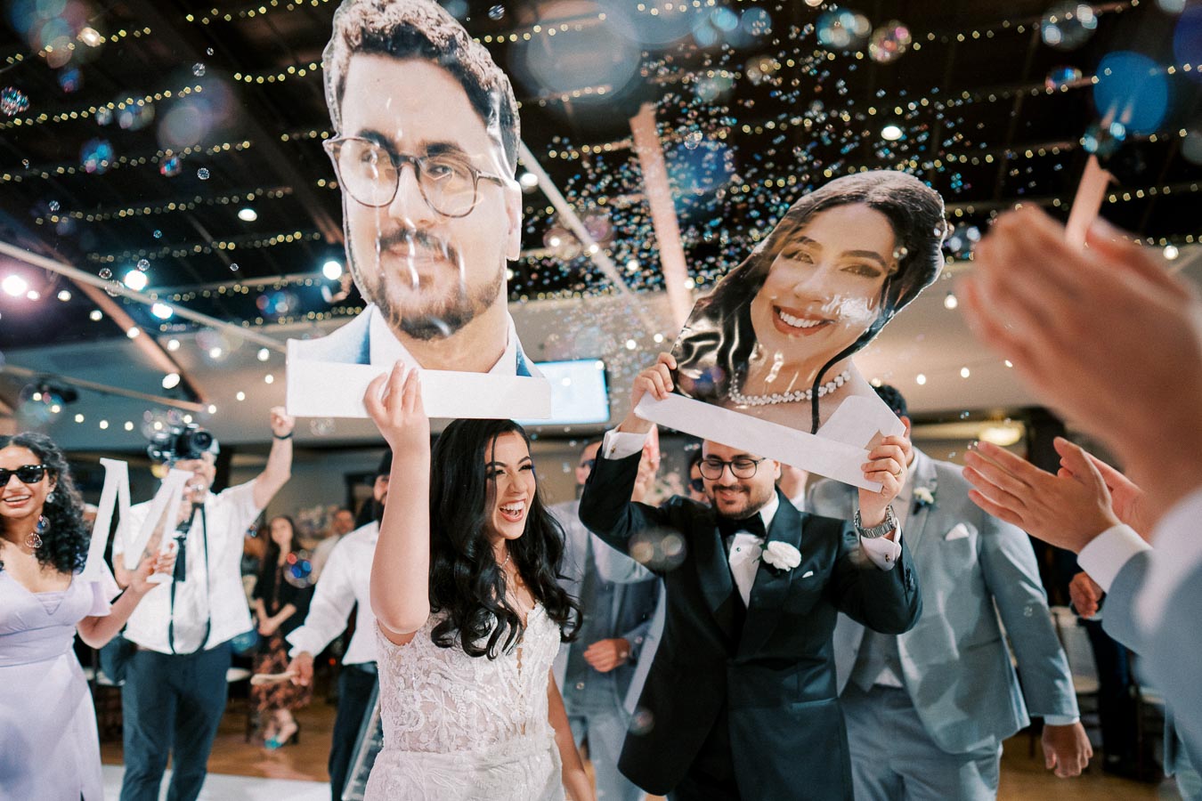 A joyous wedding reception with the bride and groom celebrating. Guests wear playful masks, surrounded by bubbles and joyful clapping, under twinkling string lights.