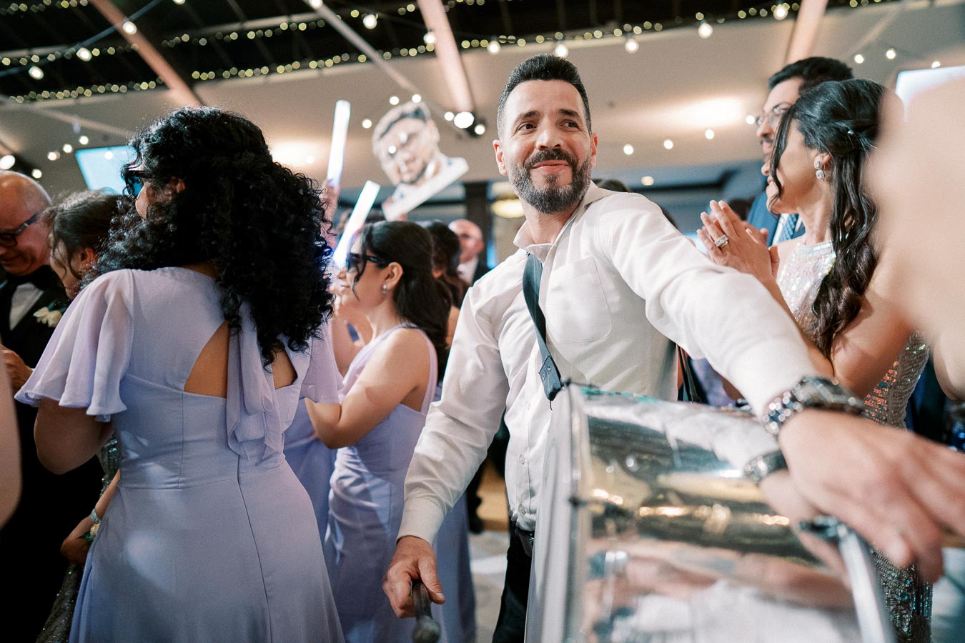 A man playing drums amidst a lively crowd at a festive celebration, with people in elegant attire dancing and enjoying the event.