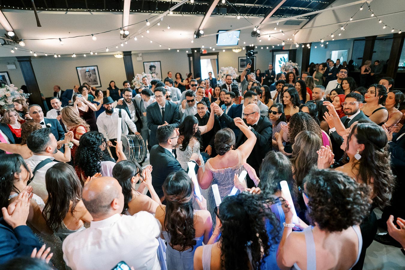 A lively wedding reception dance floor filled with guests celebrating under string lights, capturing an energetic and joyful atmosphere.