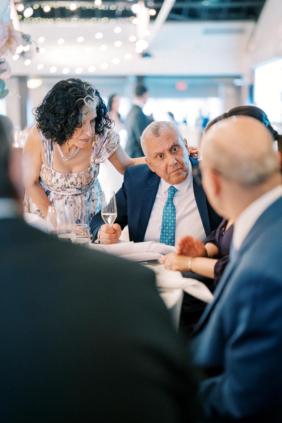 A group of elegantly dressed individuals engaged in conversation at a formal event, featuring soft lighting and ambient decorations, creating a sophisticated atmosphere.
