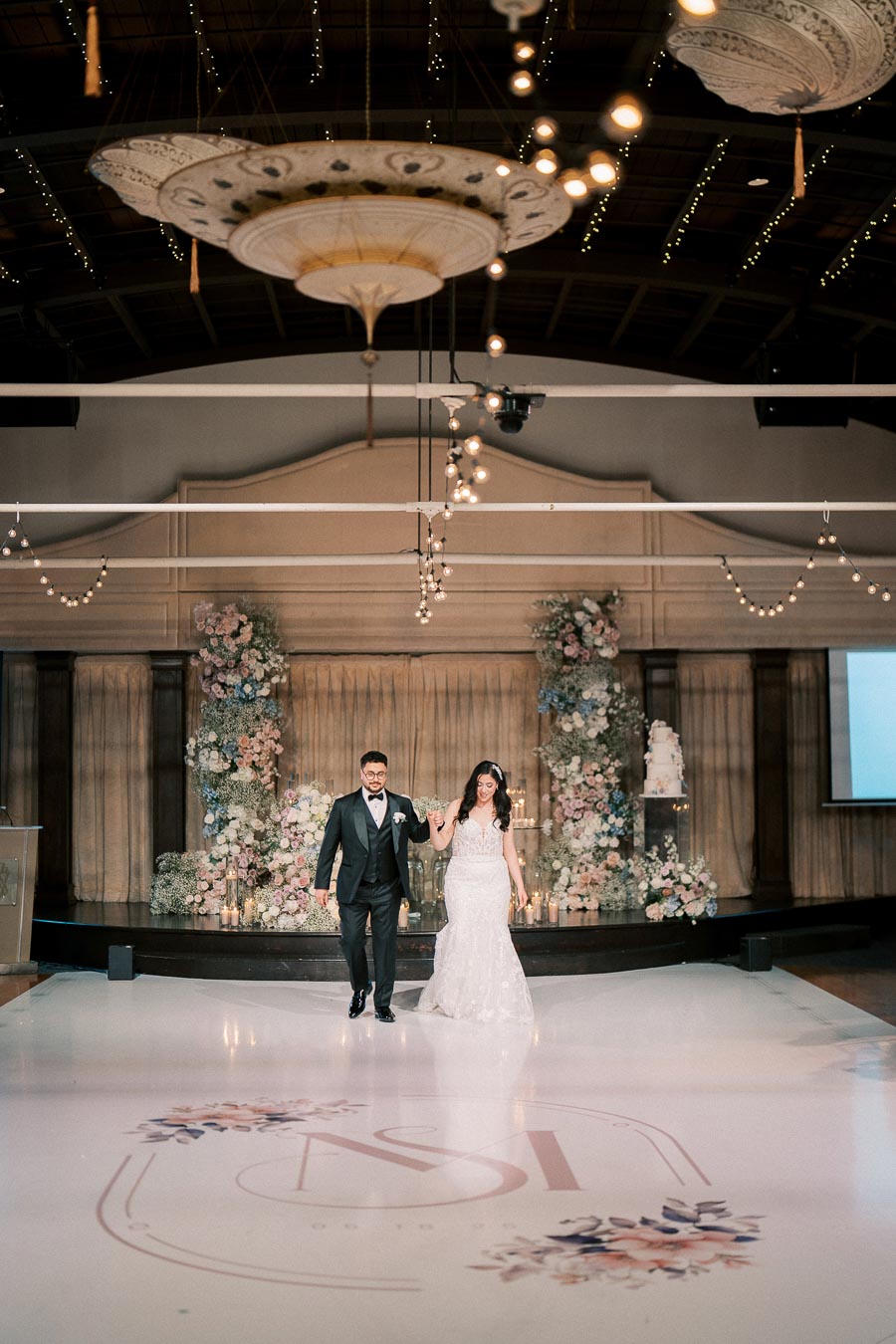 Wedding couple entering elegantly decorated reception venue, with floral arrangements and ambient lighting.