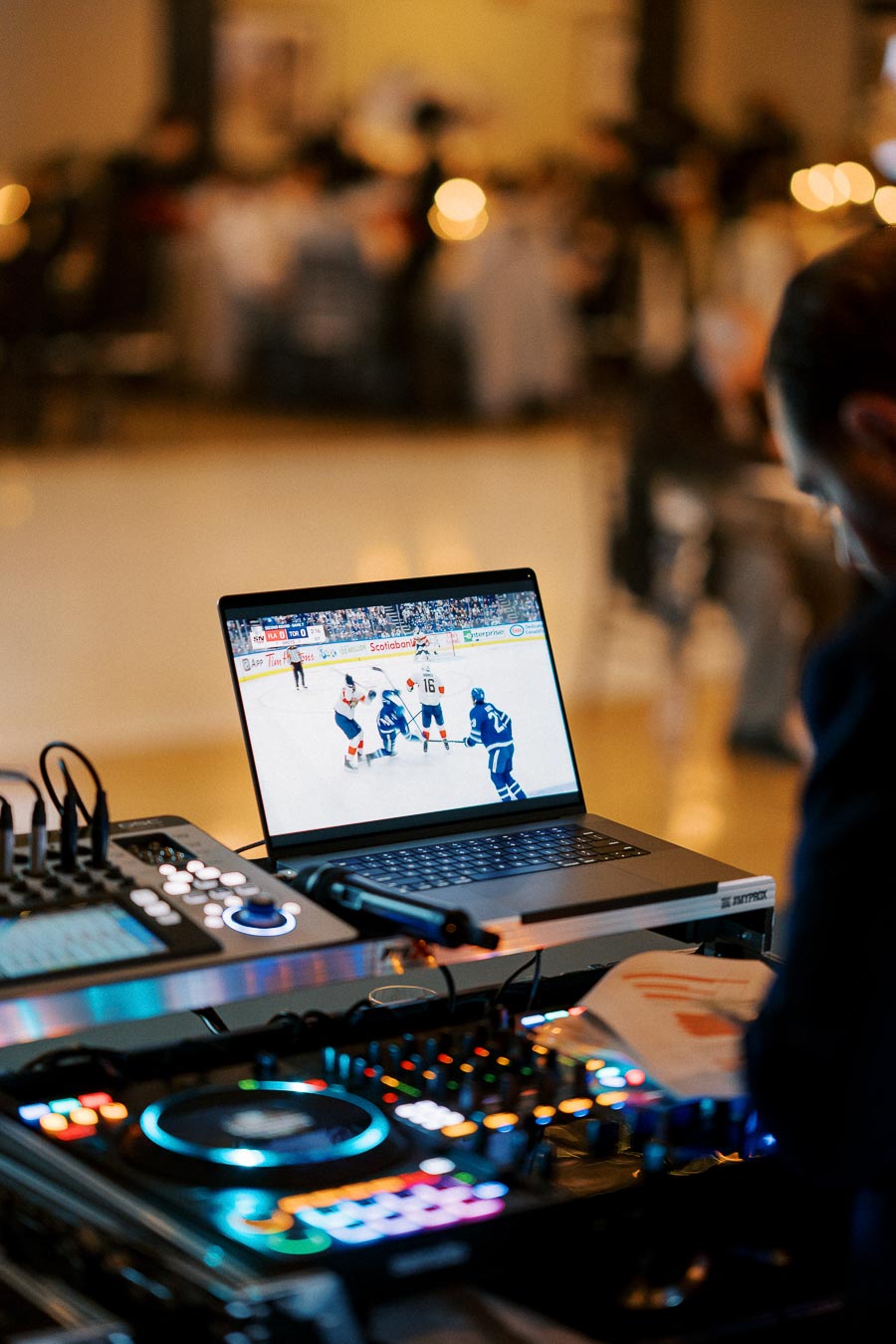 Laptop displaying a live ice hockey game next to DJ equipment at an event, combining sports entertainment with music mixing.