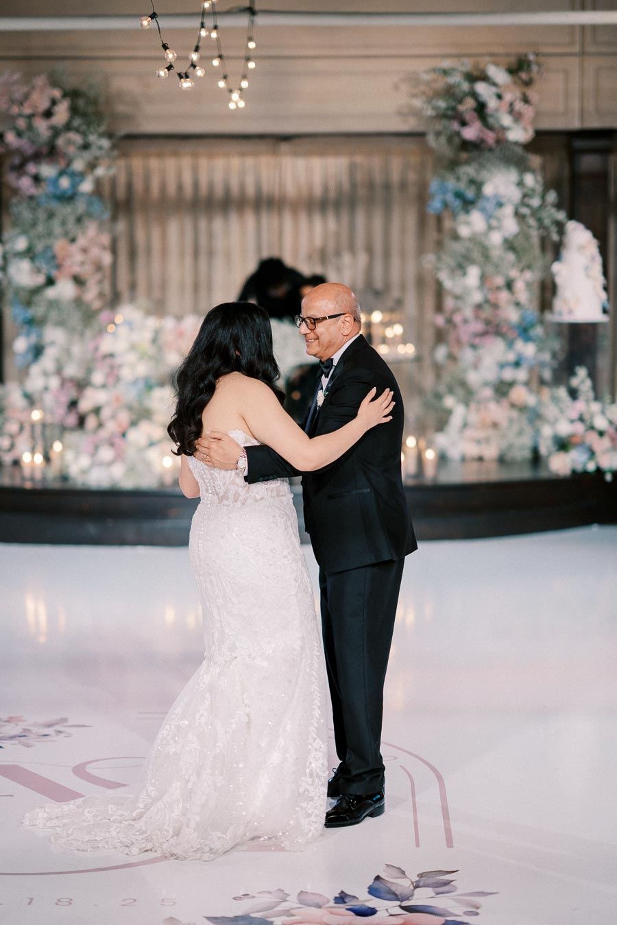 Father and bride dancing at a wedding reception, surrounded by elegant floral decorations and soft lighting.