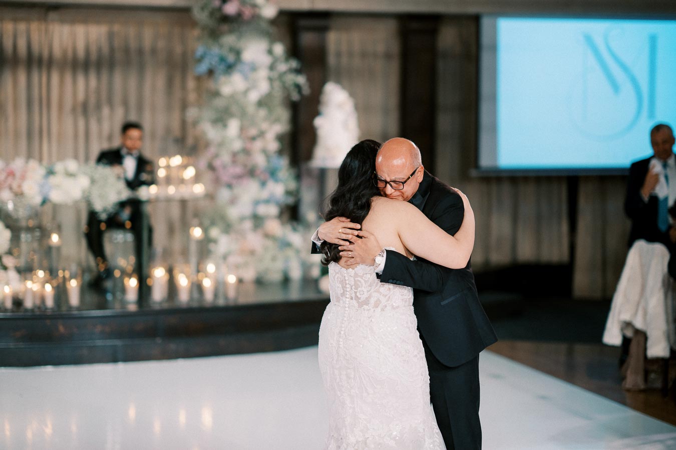 Father and bride sharing a heartfelt dance at a wedding reception, surrounded by elegant floral arrangements and candlelit ambiance.