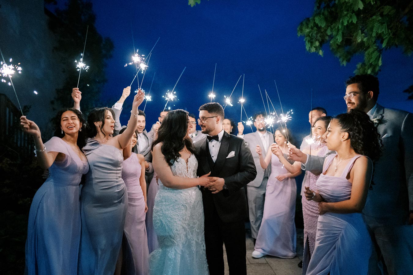 A joyful wedding celebration at night with the bride and groom surrounded by guests holding sparklers, creating a festive and romantic atmosphere.