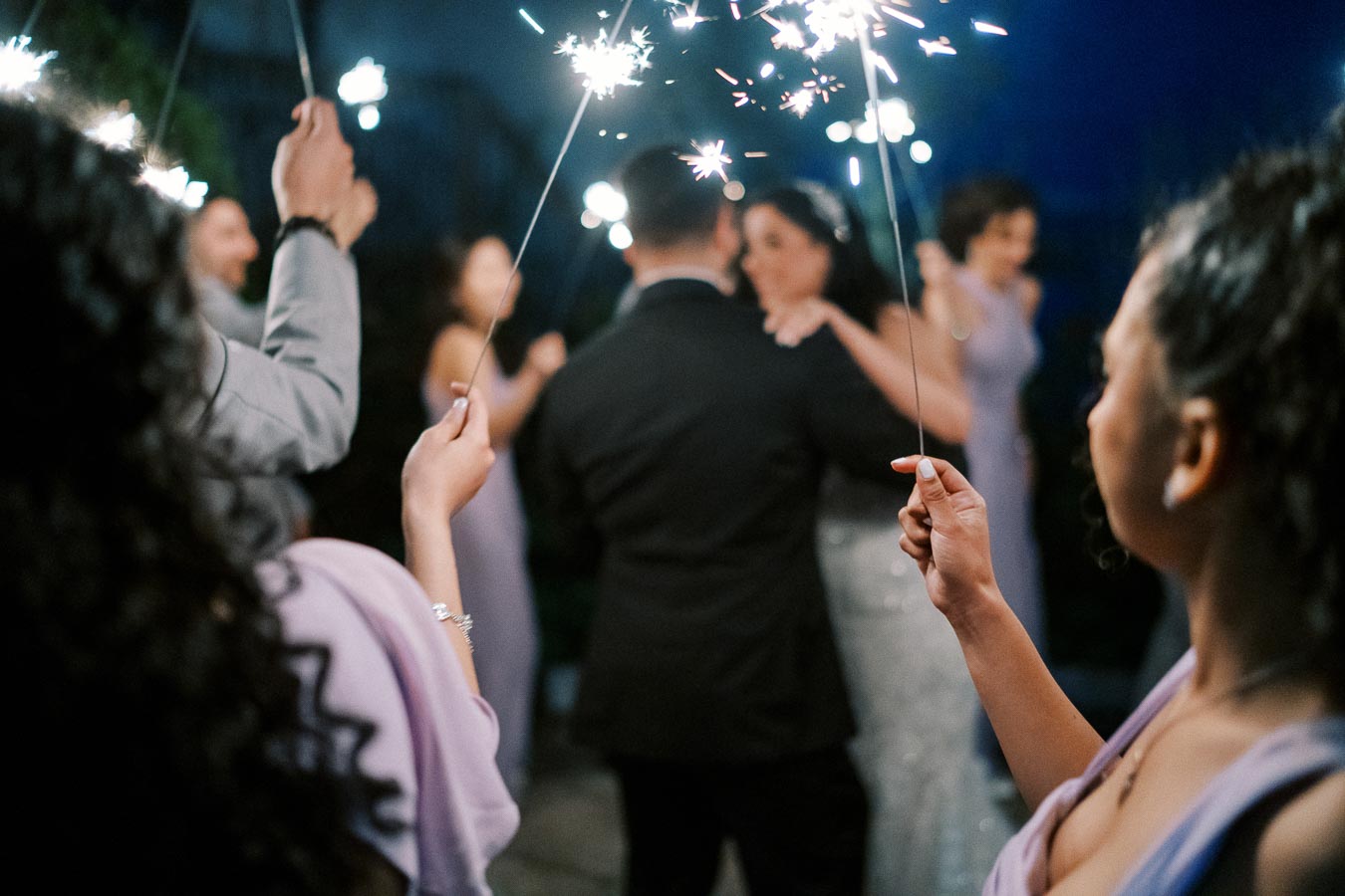 Guests holding sparklers surround a couple dancing at an outdoor evening wedding reception.