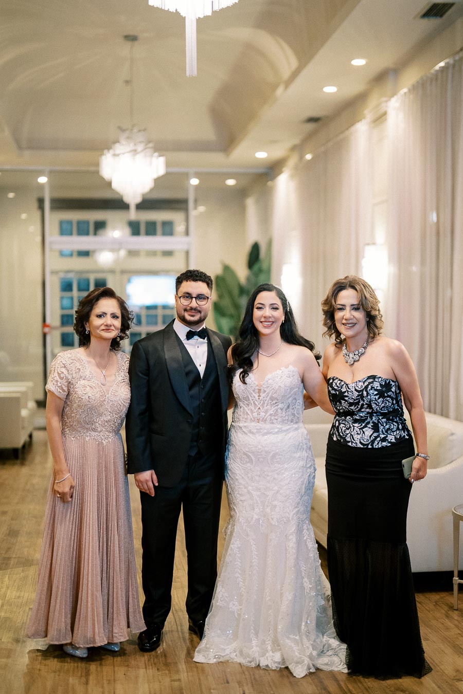 A group of four elegantly dressed people posing in a beautifully lit wedding venue.
