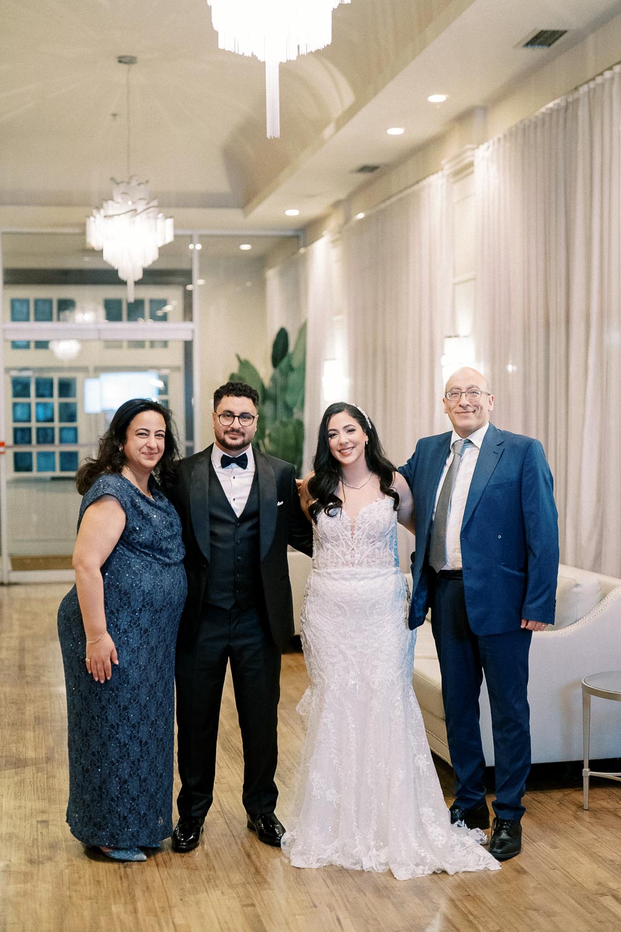 Elegant wedding couple posing with family in formal attire at a beautifully lit venue.