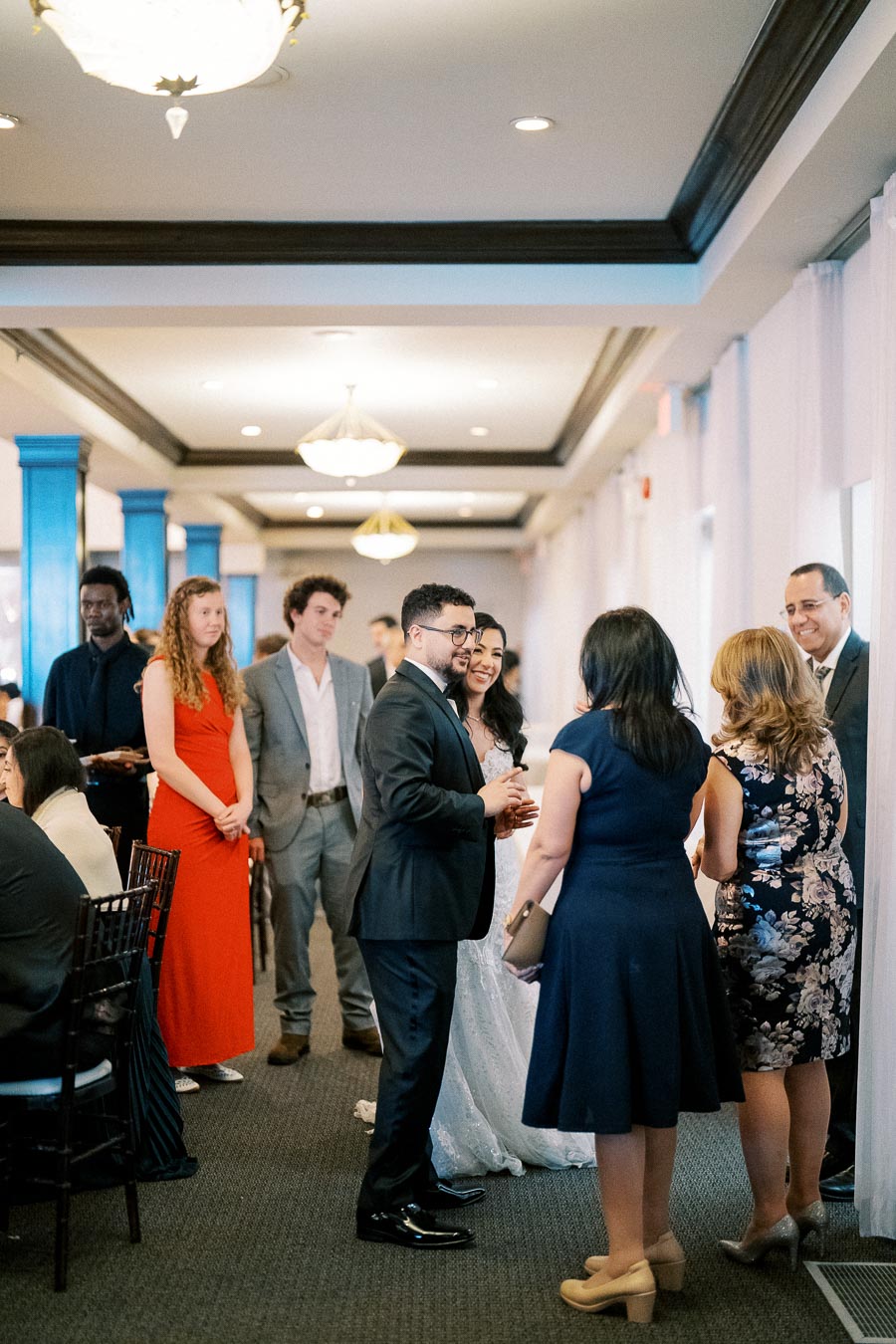 Wedding guests socializing at a reception, elegantly dressed individuals mingling in a beautifully decorated venue with chandeliers and bright lighting.