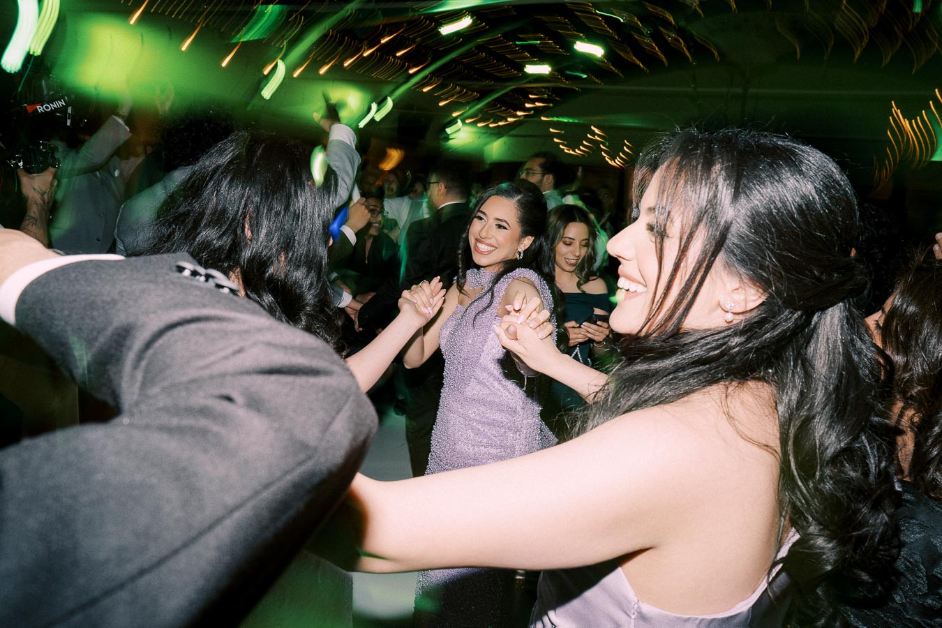 A group of joyful people dancing at a vibrant party with colorful lights, smiling and holding hands in celebration.