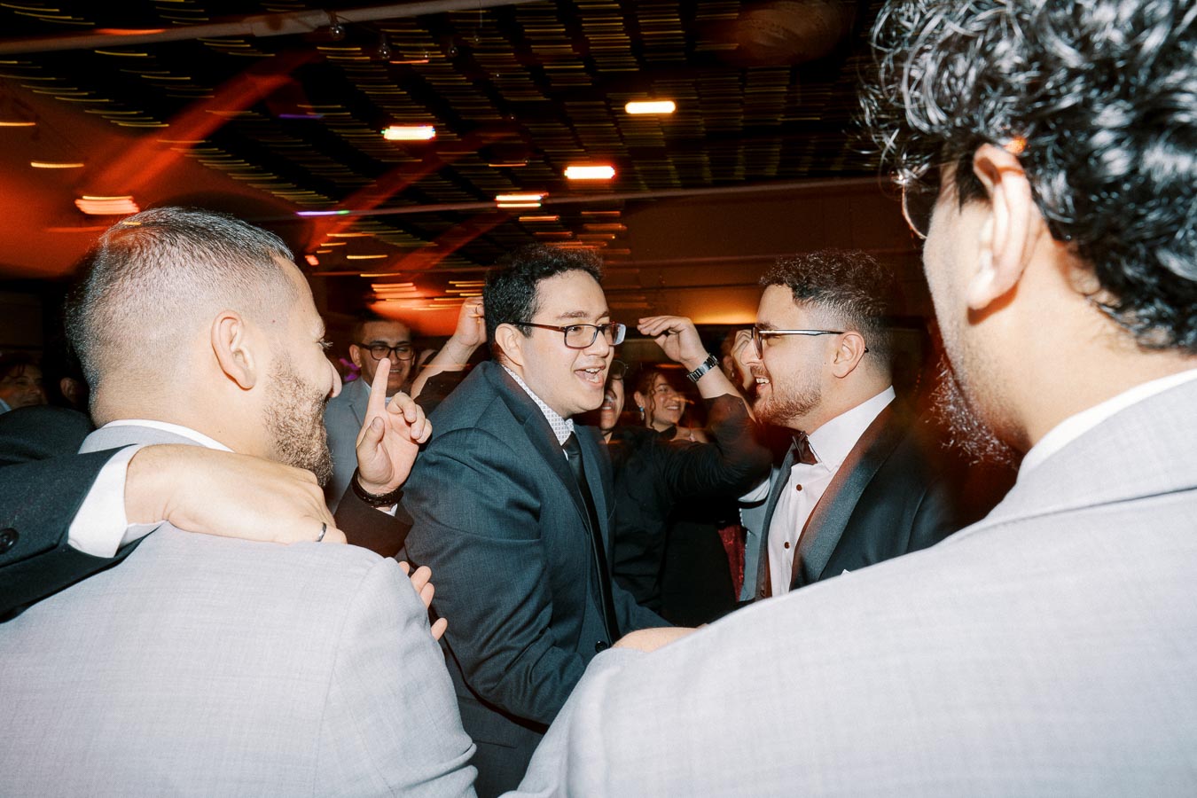 A group of people in formal attire enjoying a lively celebration indoors, with festive lighting creating a vibrant atmosphere.