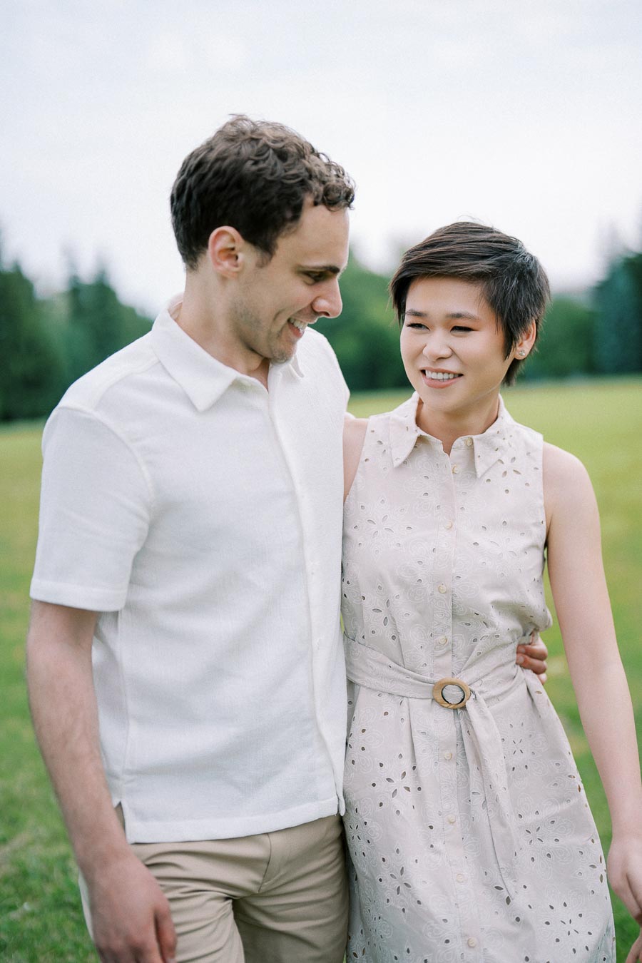 A smiling couple walking together in a green park, dressed in light summer clothing, enjoying a beautiful day outdoors.