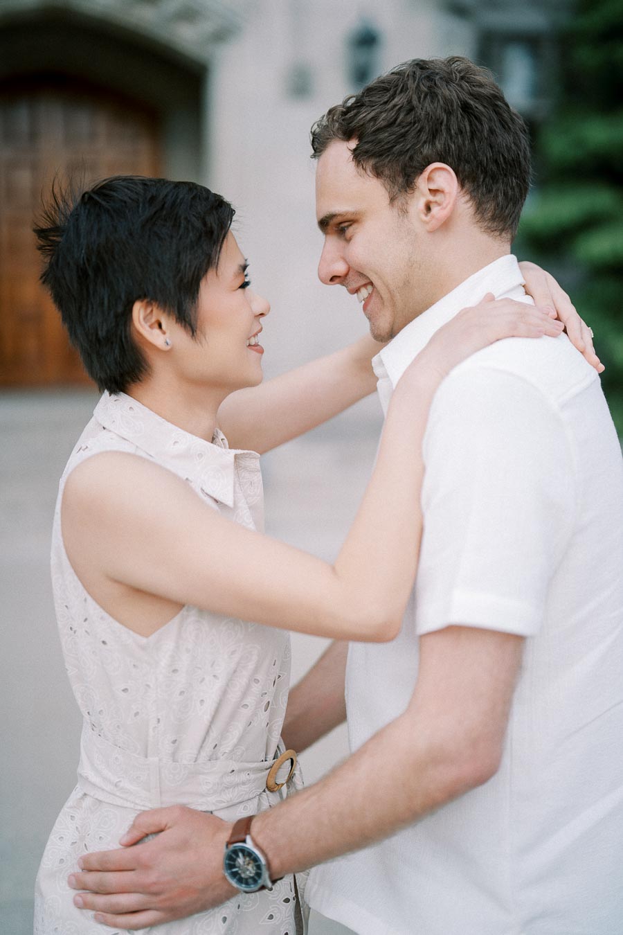 A couple embracing and smiling at each other in a romantic outdoor setting, dressed in light summer clothing.
