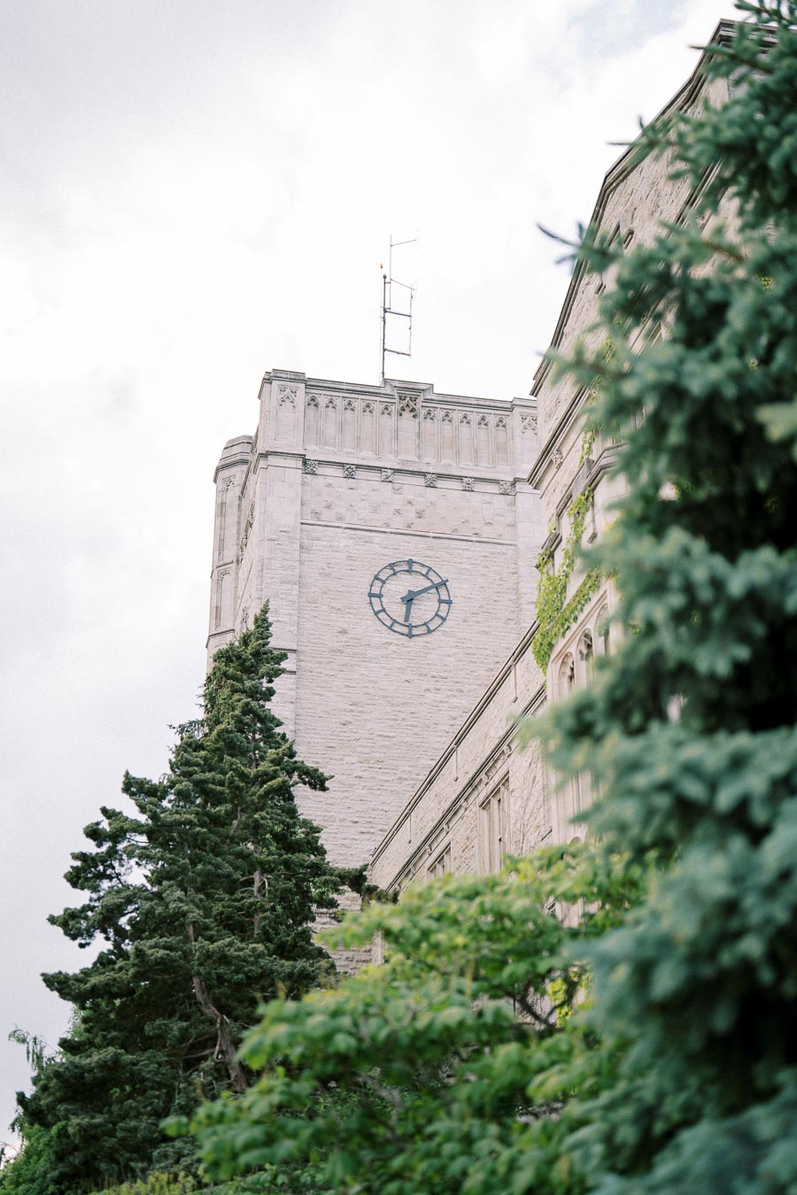 Historic stone clock tower surrounded by lush green trees under a cloudy sky