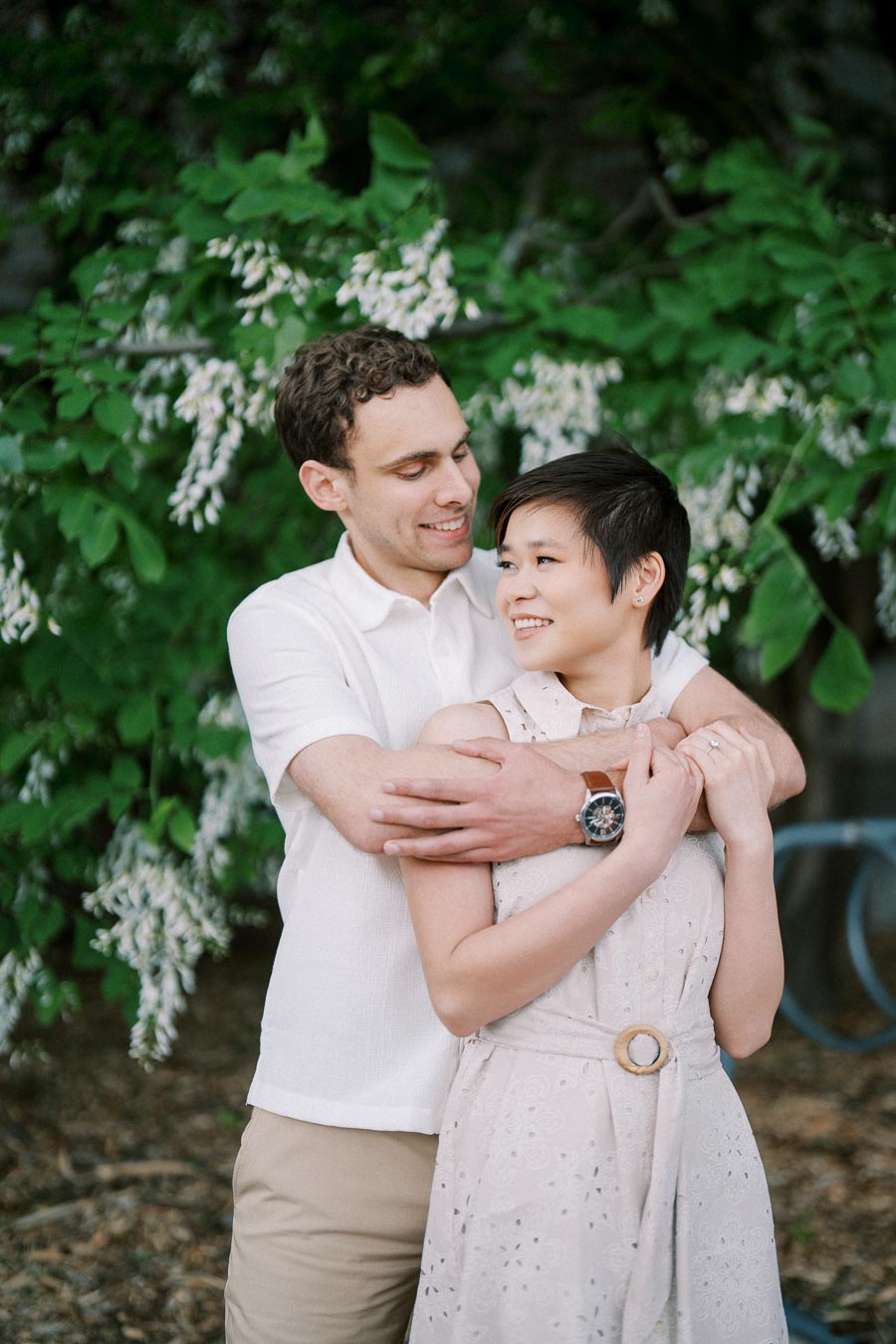 Smiling couple embracing in garden with lush greenery and white flowers in the background