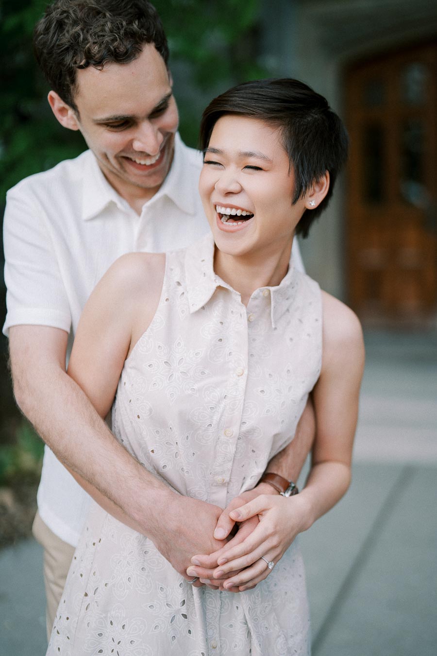 A happy couple embracing and laughing outdoors, wearing summer attire with soft natural lighting.
