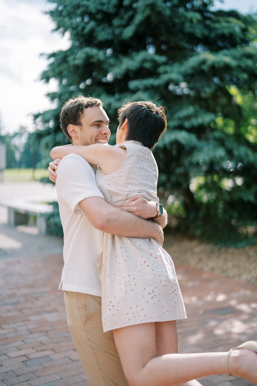 A joyful couple embracing romantically outdoors on a sunny day, surrounded by lush greenery.