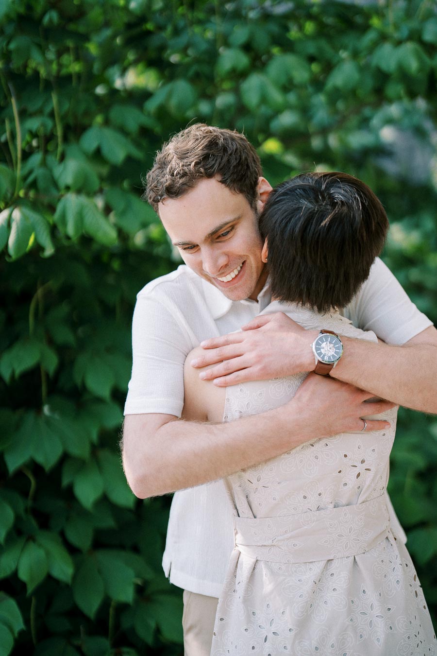 A happy couple embracing in a lush green garden, one person smiling warmly while wearing a white shirt and wristwatch.