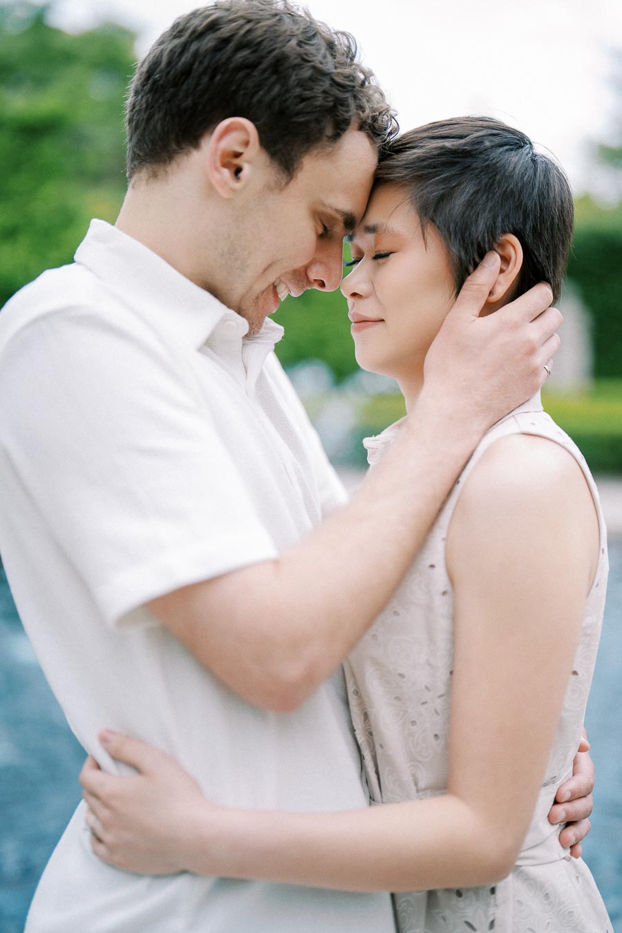 A couple embracing outdoors, with a serene expression, showcasing love and affection on a sunny day.