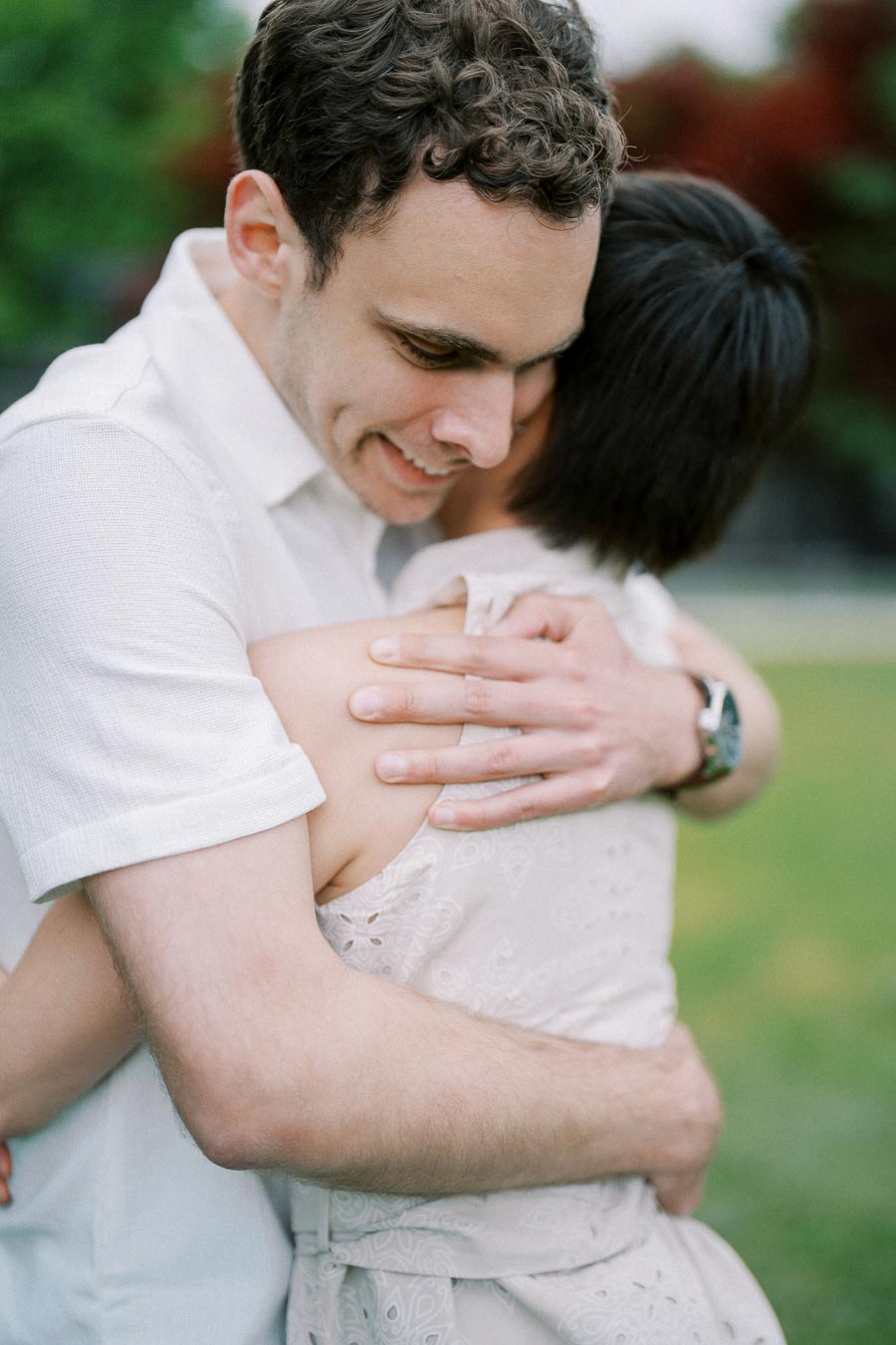 A couple embracing warmly in a park setting, showcasing love and affection, with greenery in the background.