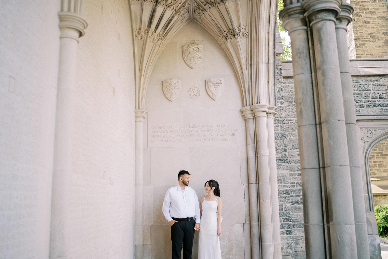 A couple stands together in an elegant stone archway, gazing at each other lovingly, capturing a romantic moment in a historic setting.