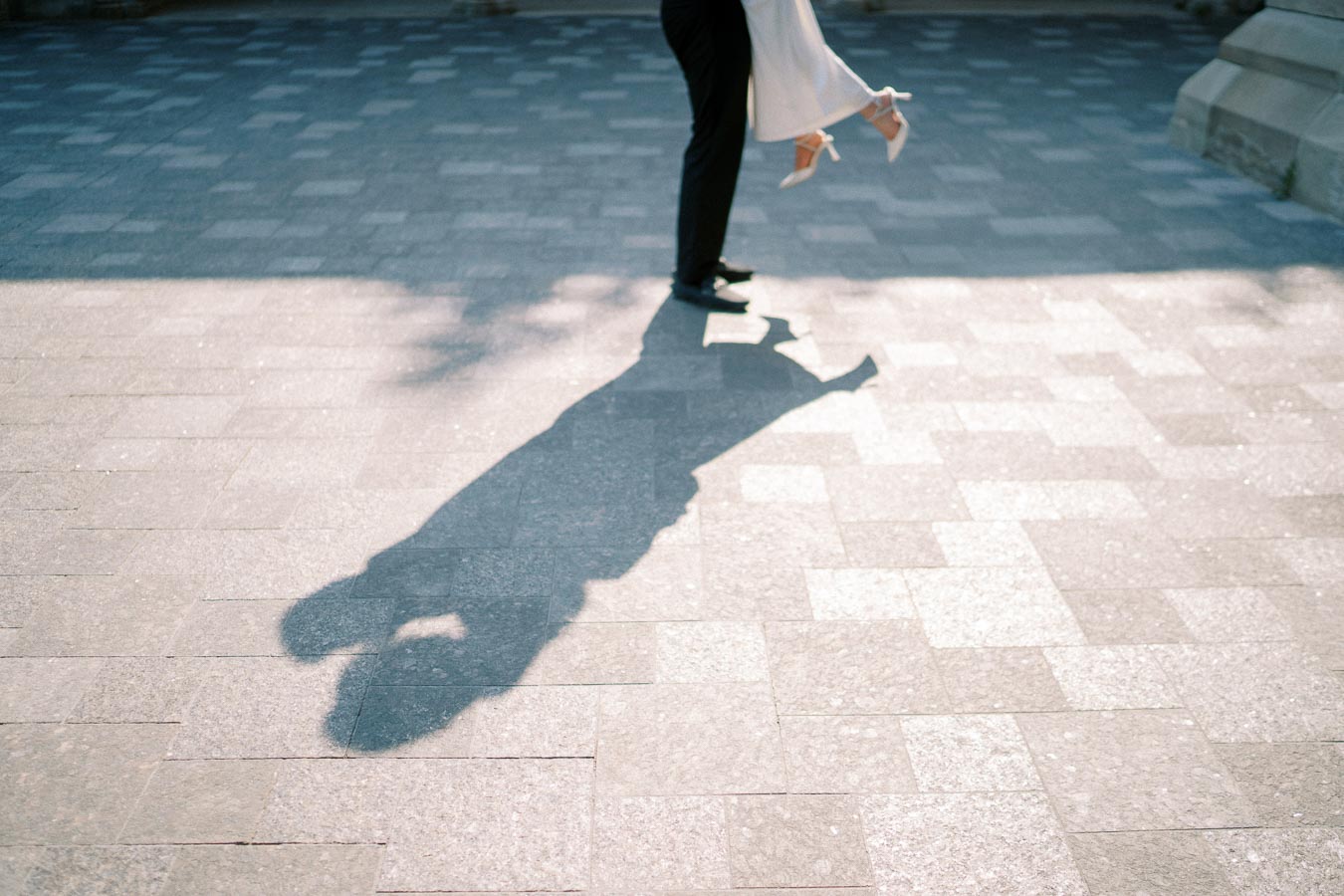 Shadow of a couple embracing on a sunlit stone pavement, with one partner lifting the other off the ground, creating a romantic and playful scene.