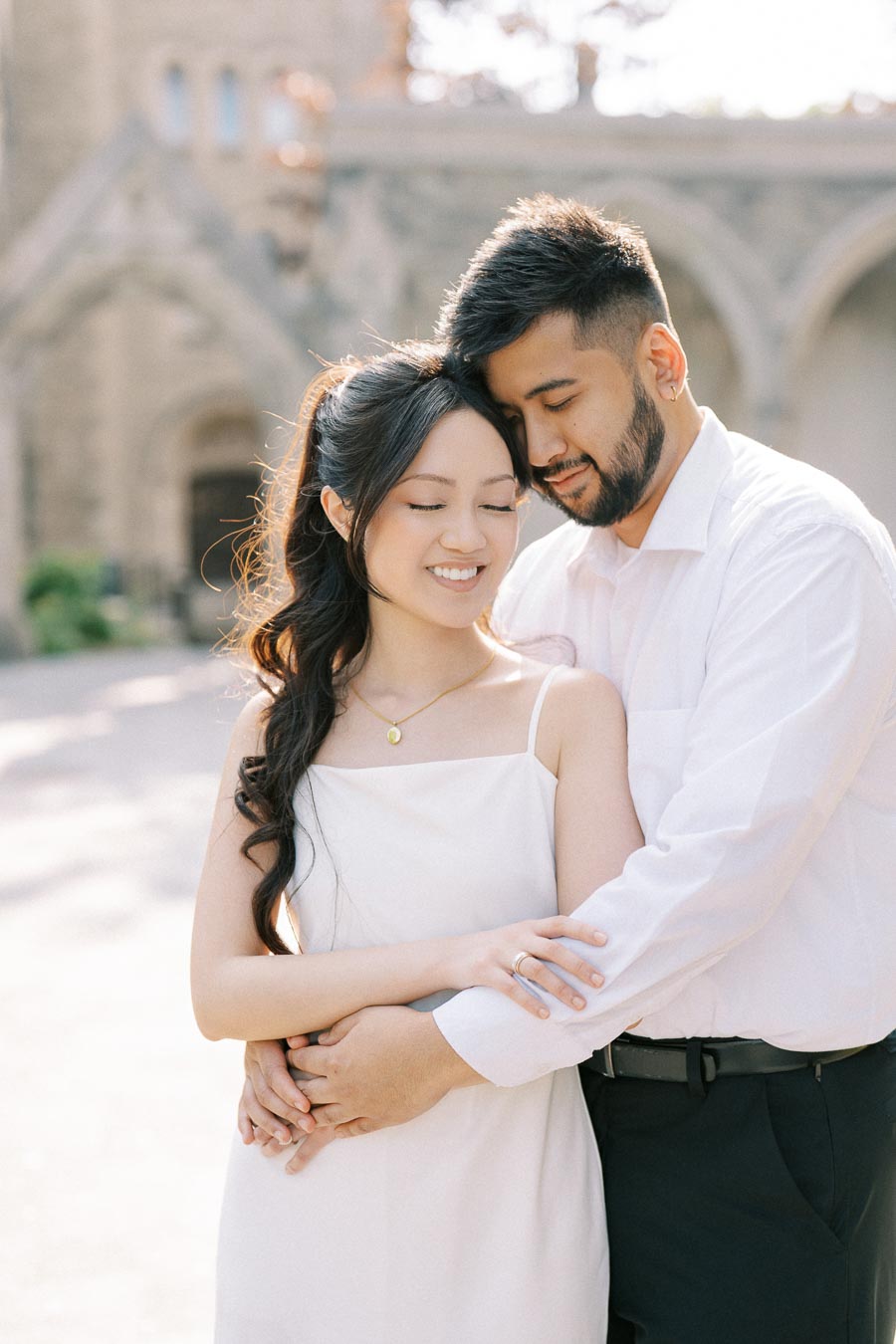 A happy couple in elegant attire embracing gently in front of a historic building, conveying love and romance.