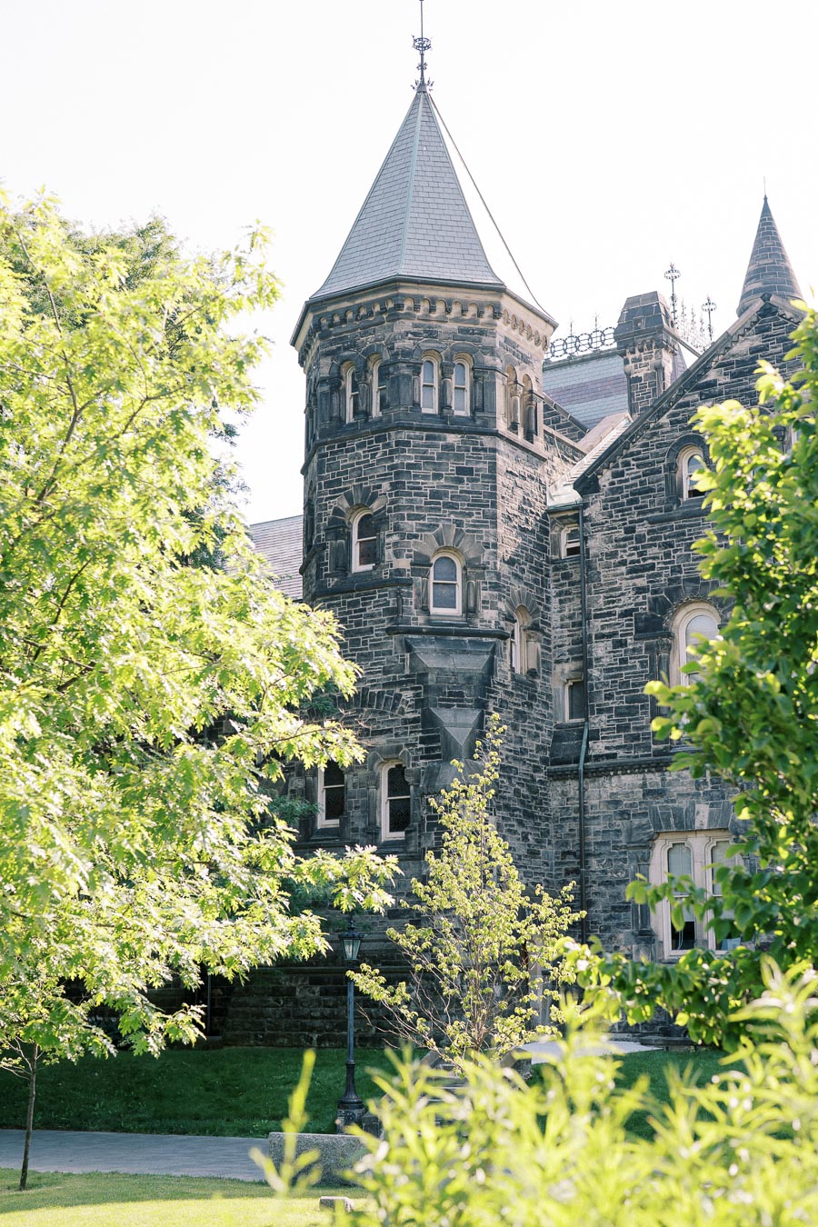Historic stone castle-like building with turret surrounded by lush green trees on a sunny day