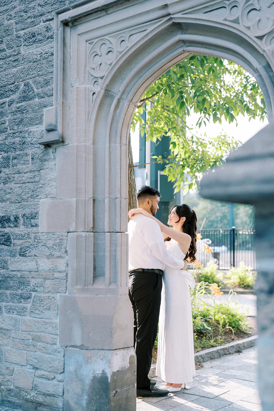 Romantic couple embracing under a stone archway in a sunlit garden.