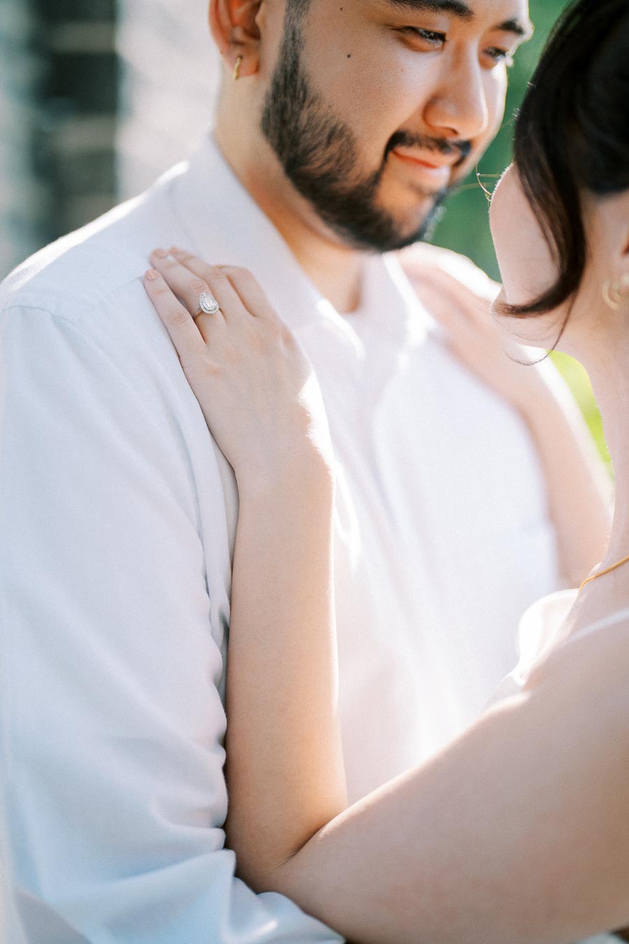 A couple embracing in a romantic setting, with focus on the woman's engagement ring on her finger, capturing an intimate moment of love and commitment.