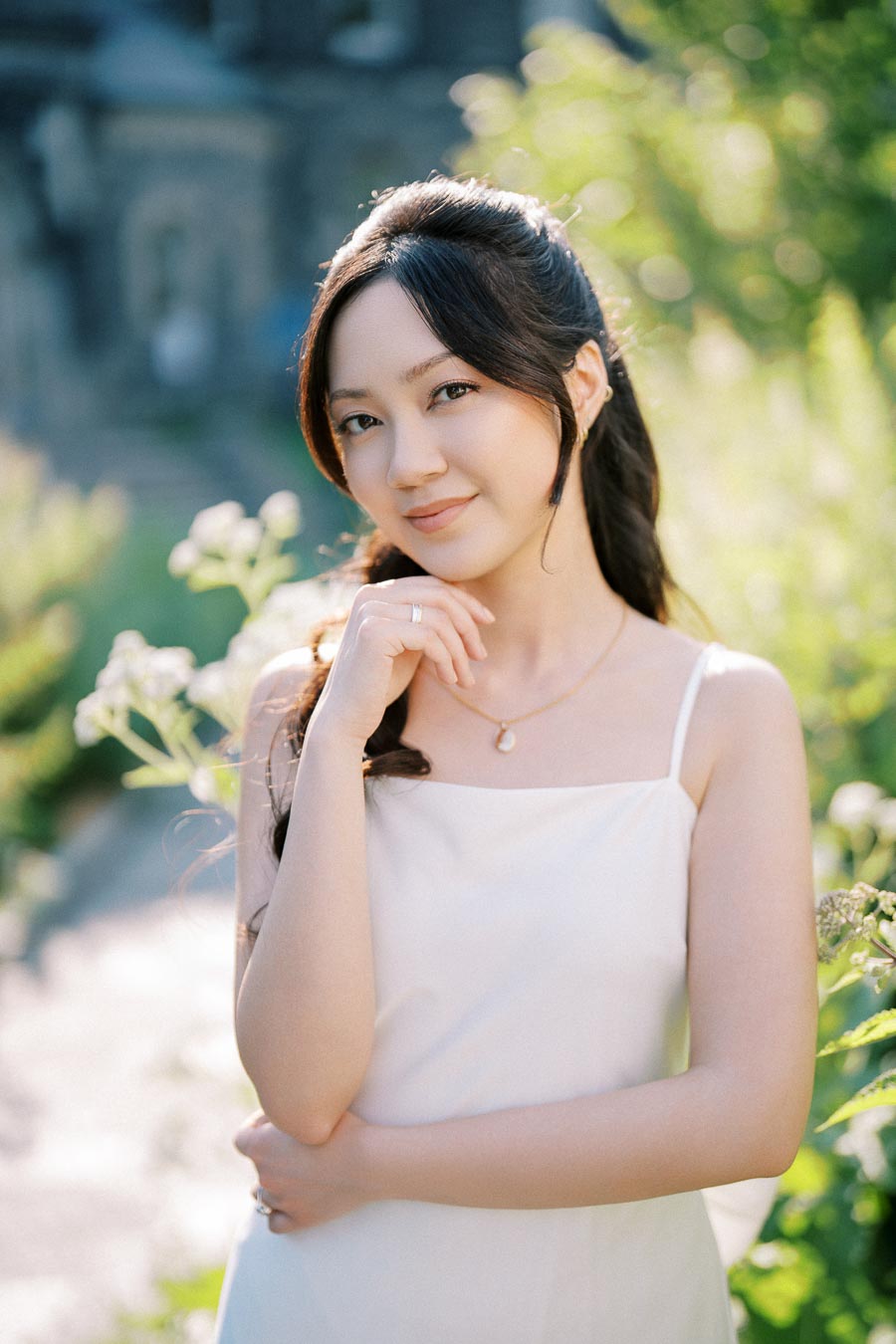 Young woman in a white dress posing outdoors in a sunny garden setting.