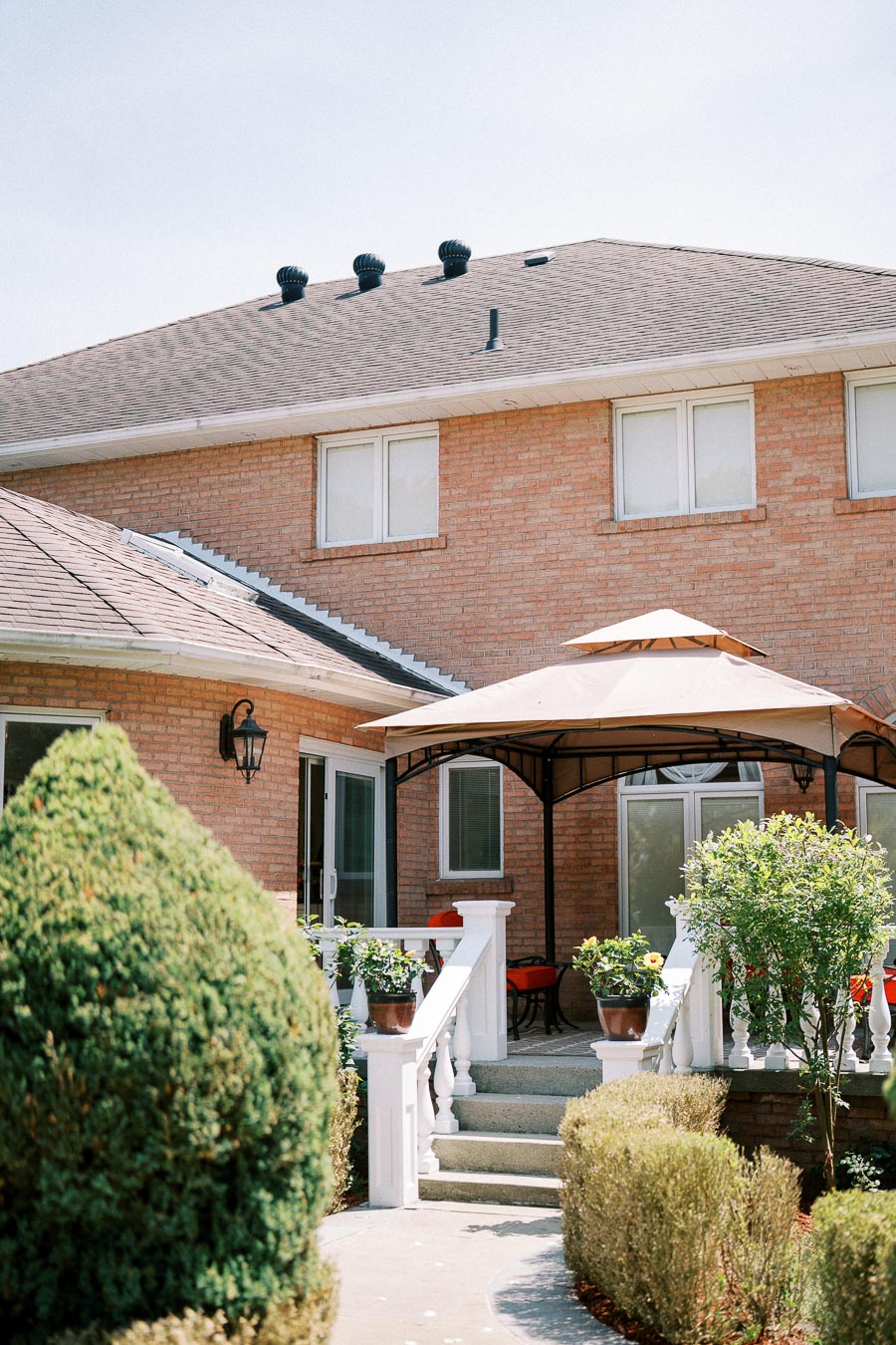 Backyard view of a modern brick house featuring a cozy patio area with a gazebo and outdoor furniture, surrounded by lush greenery and manicured shrubs.