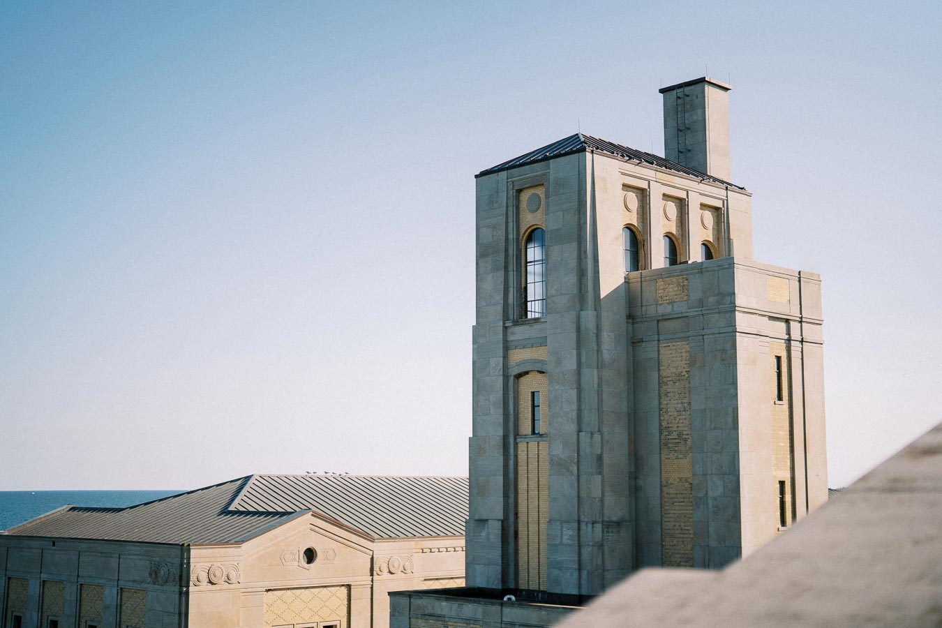 Historic stone building with arched windows and intricate details, set against a clear blue sky near a waterfront.