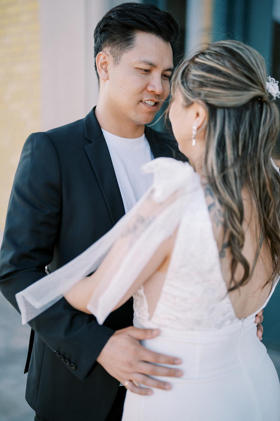 Couple in elegant wedding attire embracing each other, creating a romantic and intimate moment outdoors.