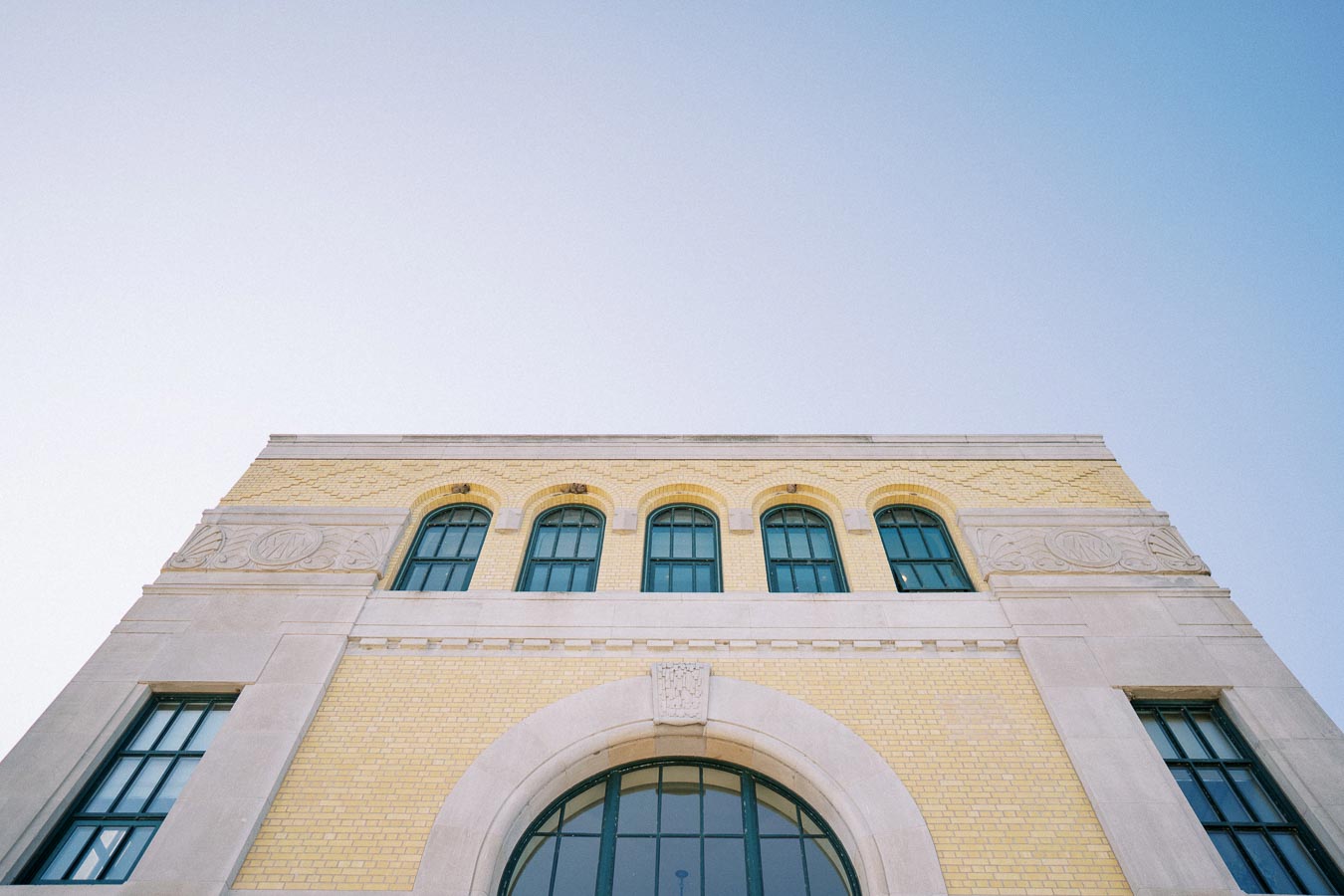 Low-angle view of a historical building facade with yellow brick and arched windows against a clear sky.