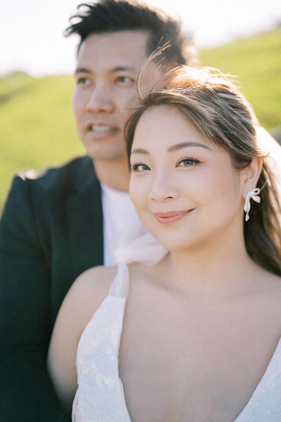 Smiling couple posing together outdoors on a sunny day, woman in white dress with nature background