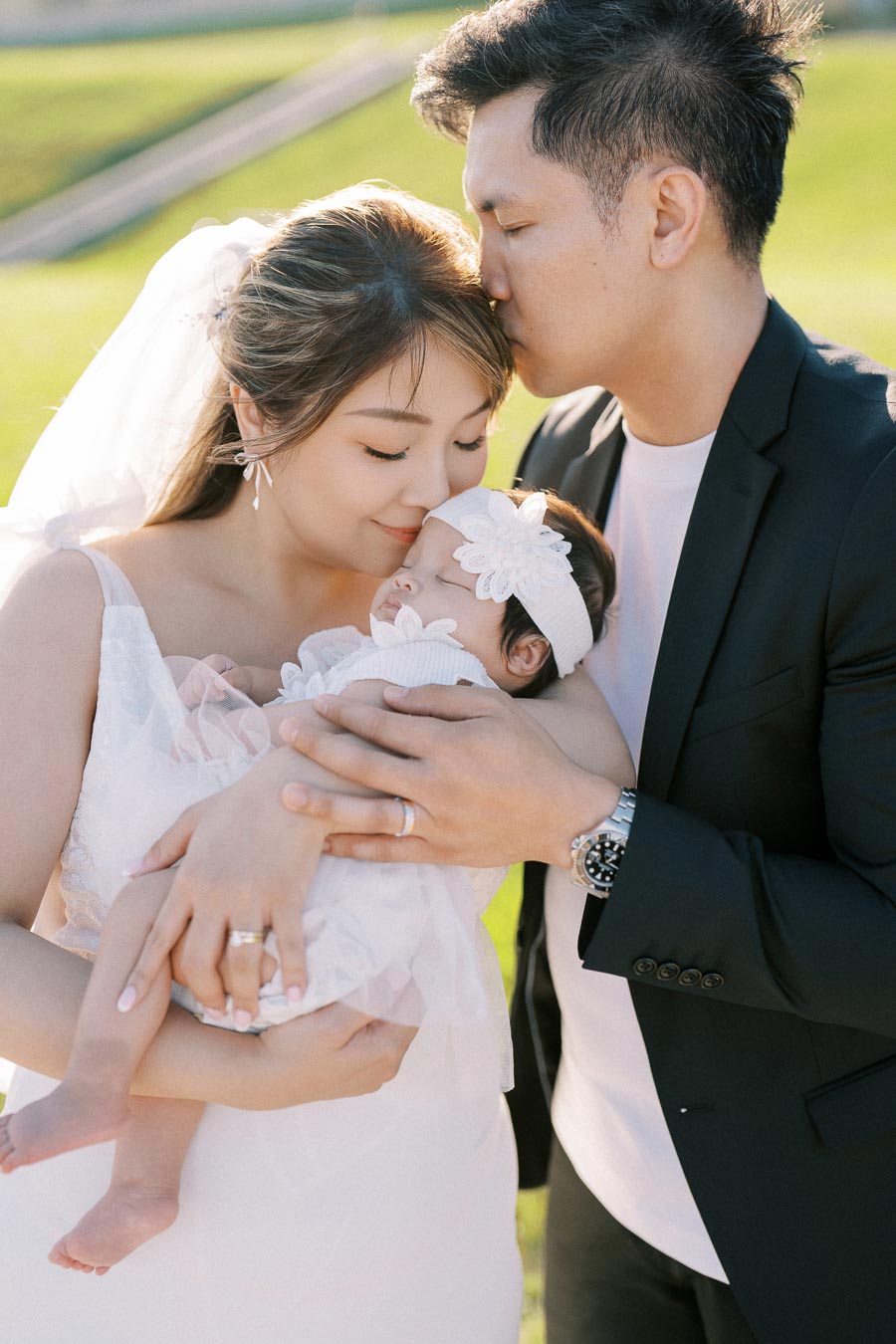 A loving couple embraces their sleeping newborn in an outdoor setting, capturing a heartwarming family moment.